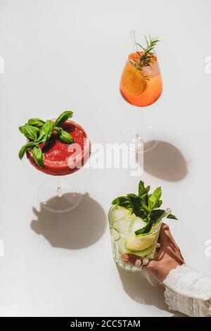 Beliebte Bar Sommer Eis alkoholische Cocktails. Gin-Tonic, Aperol Spritz und Erdbeerbasil Margarita in Gläsern und Womans Hand hält Glas über Plai Stockfoto