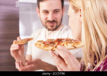 Glückliches Paar essen ihre hausgemachte und leckere Pizza in der Küche Stockfoto