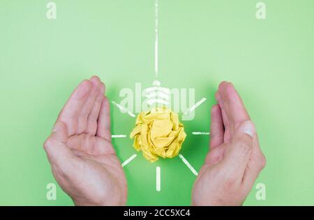 Energieeinsparung und Nachhaltigkeit Konzept, Hände Abschirmung gelben Papier Glühbirne auf grünem Hintergrund Stockfoto