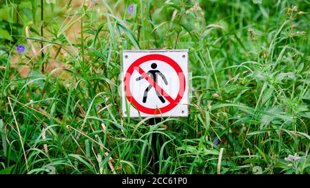 Rotes rundes Verbotsschild mit einer schwarzen Silhouette eines durchgestrichenen Mannes. Verbot, auf dem Gras zu laufen. Panoramaformat Stockfoto