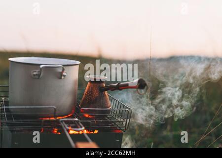 Metalltopf und türke auf dem Feuer. Morgenkaffee auf dem Campingplatz im Freien Stockfoto