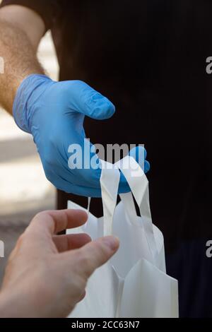 Vertikale Aufnahme eines Liefermanns in einer Schutzmaske Und medizinische Handschuhe mit einem Papierbeutel Stockfoto