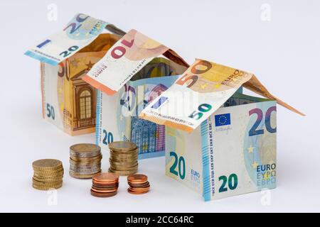 Häuser aus 10, 20 und 50 Euro-Banknoten, Stapel von Euro-Münzen, weißer Hintergrund. Konzepte von Preisen und Kosten im Zusammenhang mit Wohnen und Immobilien Stockfoto