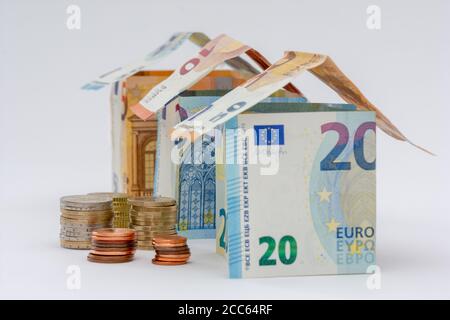 Häuser aus 10, 20 und 50 Euro-Banknoten, Stapel von Euro-Münzen, weißer Hintergrund. Konzepte von Preisen und Kosten im Zusammenhang mit Wohnen und Immobilien Stockfoto