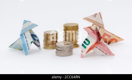 Drei Origami-Vögel aus 10, 20 und 50 Euro-Banknoten, um Stapel von Euro-Münzen, weißer Hintergrund Stockfoto