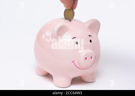 Hand, die eine 2-Euro-Münze in ein Sparschwein. Sparen Geld und Finanzen Konzept. Weißer Hintergrund Stockfoto