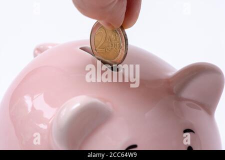 Hand, die eine 2-Euro-Münze in ein Sparschwein. Sparen Geld und Finanzen Konzept. Weißer Hintergrund Stockfoto