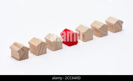 Winzige Holzspielzeughäuser in einer Reihe, das in der Mitte rot bemalte, weiße Hintergrund Stockfoto