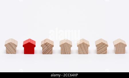 Winzige Holzspielzeughäuser in einer Reihe, eines davon mit rotem, weißem Hintergrund Stockfoto