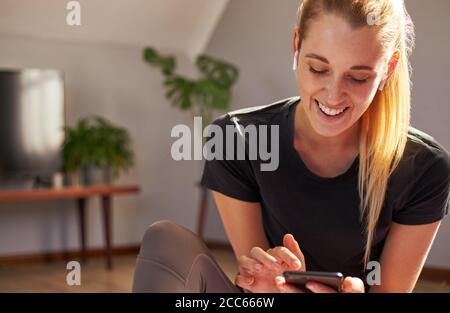 Junge Frau, die Smartphone benutzt, während sie zu Hause mit Ohrhörern arbeitet. Stockfoto