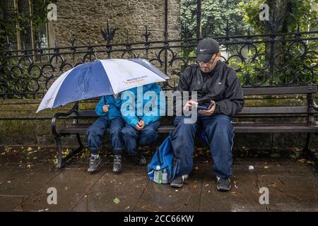 Tenby, West Wales. August 2020. UK Wetter: Tenby, West Wales. August 2020. Eine Familie deckt sich vom Wetter, während sie auf einer Bank sitzt, die einen Schirm in Tenby, West Wales, Pembrokeshire während eines Sommertages teilt, stoms und schlechtes Wetter traf Südengland und West Wales, Vereinigtes Königreich. Mittwoch, 19. August 2020. Tenby, Pembrokeshire, West Wales, UK Kredit: Jeff Gilbert/Alamy Live News Stockfoto