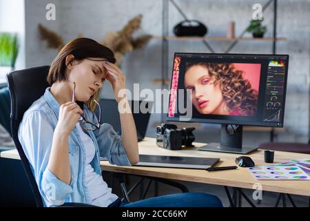 Porträt von müde Grafikdesigner arbeiten Überstunden im Büro. Gestresste Arbeiter haben Augenstrapazheitssymptome. Retoucher Arbeitsplatz im Fotostudio. Burnout Stockfoto