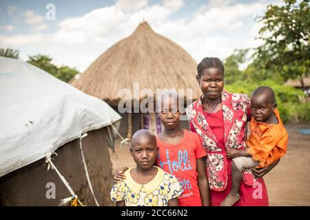 Eine Flüchtlingsfamilie aus dem Südsudan - eine Mutter und ihre drei Kinder - stehen vor ihrem Haus in Palabek Flüchtlingssiedlung im Norden Ugandas, Ostafrika. Stockfoto