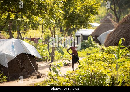 Flüchtlinge aus dem Südsudan leben in behelfsmäßigen, mit Planen bedeckten Lehmhäusern und Grasbüschel-Häusern in der Palabek-Flüchtlingssiedlung im Norden Ugandas, Ostafrika. Stockfoto