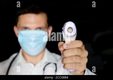 Coronavirus Symptome, Mann in medizinische Maske misst Körpertemperatur. Arzt mit einem digitalen isometrischen berührungslosen Thermometer in der Hand Stockfoto