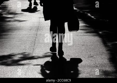 Silhouette und Schatten der Frau, die auf einer Straße geht. Weibliche Beine auf einem Bürgersteig, Konzept der Quarantäne in der Stadt während der Coronavirus-Pandemie Stockfoto