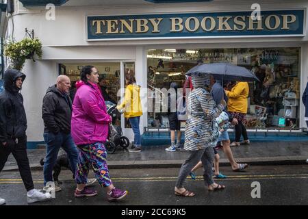 Tenby, West Wales. August 2020. UK Wetter: Touristen Schlange im Regen vor einem Buchladen auf der Hauptstraße in Tenby auf der Suche nach alternativen Dingen zu tun. Während der Post-Lockdown Touristen haben eine Menge von Attraktionen noch für Besucher in West Wales geschlossen gefunden. Stürme und schlechtes Wetter trafen Südengland und Westwales während der Nacht und hielten bis in den Tag Touristen von den Stränden in Pembrokeshire, Großbritannien ab. Mittwoch, 19. August 2020. Tenby, Pembrokeshire, West Wales, UK Kredit: Jeff Gilbert/Alamy Live News Stockfoto