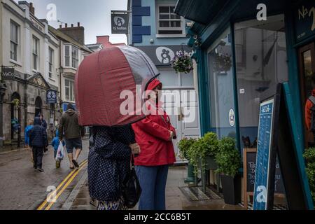 Tenby, West Wales. August 2020. UK Wetter: Zwei Frauen Schlange im Regen vor einem Café auf der Hauptstraße in Tenby, Pembrokeshire tragen soziale distanzierende nasse Wetter Kleidung. West Wales wurde über Nacht und während des folgenden Sommertages mit Regenstürmen und schlechtem Wetter getroffen, Großbritannien. Mittwoch, 19. August 2020. Tenby, Pembrokeshire, West Wales, UK Kredit: Jeff Gilbert/Alamy Live News Stockfoto