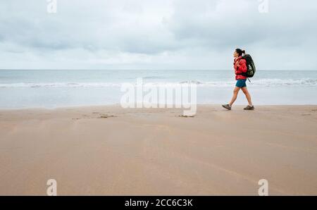 Frau Reisende gehen an regnerischen Tagen auf leerem Meeresstrand Stockfoto