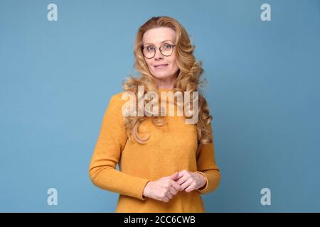 Frau, die auf die Kamera schaut und lächelt, während sie vor blauem Hintergrund steht. Stockfoto