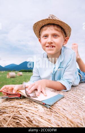 Junge mit Buch liegt auf der Heurolle Stockfoto