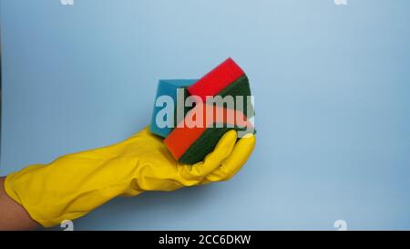 Hand in Handschuh hält wenige Waschschwämme auf blauem Hintergrund - Menge der Hausarbeit Konzept, Stockfoto