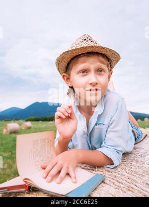 Junge liegt auf Heurolle zwischen dem Bergfeld und Liest ein Buch Stockfoto