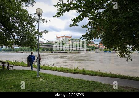 Bratislava, Slowakei - 5. Juli 2020: Menschen, die auf einem Fußweg an der Donau in Bratislava spazieren, mit der Burg auf dem Hügel im Hintergrund Stockfoto