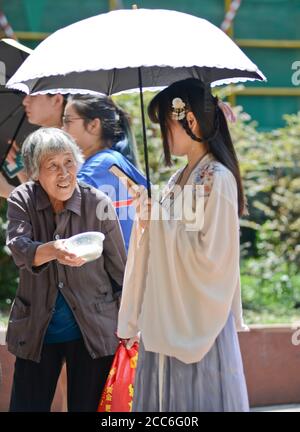 Wuhan: Eine alte chinesische Dame bittet in der Jianghan Straße um Geld für ein junges Mädchen, das in traditioneller Kleidung gekleidet ist. China Stockfoto