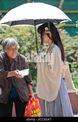 Wuhan: Eine alte chinesische Dame bittet in der Jianghan Straße um Geld für ein junges Mädchen, das in traditioneller Kleidung gekleidet ist. China Stockfoto