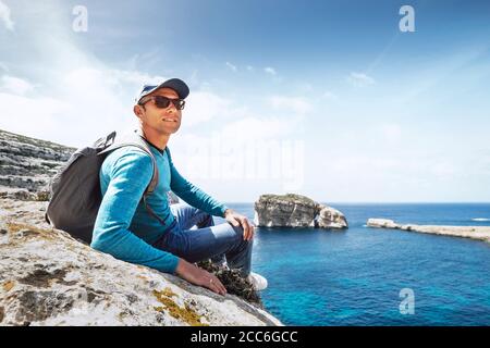 Mann mit Rucksack sitzt auf dem felsigen Meer Stockfoto