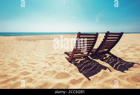 Zwei Liegen am leeren Meeresstrand unter der strahlend leuchtenden Sonne Stockfoto