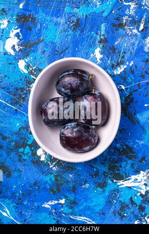 Frische süße Pflaumenfrüchte in weißer Schale auf blauem abstrakten Hintergrund, Draufsicht Stockfoto