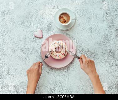 Weibliche Hände mit Gabel und Messer schneiden Donut Form Keks Stockfoto