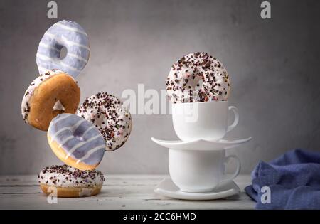 Stillleben mit fallenden Donuts und weißen Tassen Stockfoto
