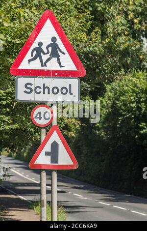 Ländliche Land Schule dreieckiges Warnschild in Straßenhecke. UK Junge und Mädchen zu Fuß Piktogramm für Sicherheitsbewusstsein. Metapher zurück in die Schule. Stockfoto