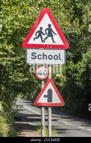 Ländliche Land Schule dreieckiges Warnschild in Straßenhecke. UK Junge und Mädchen zu Fuß Piktogramm für Sicherheitsbewusstsein. Metapher zurück in die Schule. Stockfoto