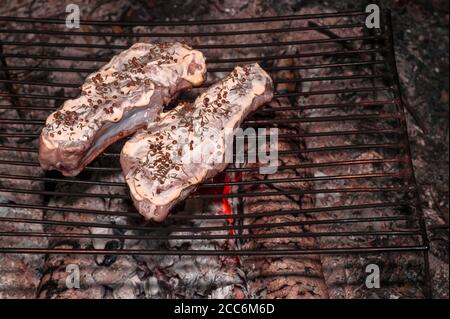 Die Schweinefilets roh auf der Rippe in der Soße mit den Gewürzen werden auf dem Grill zum Kochen auf den Kohlen gelegt. Hintergrund. Stockfoto