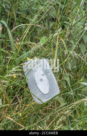 Plastikbehälter zum Mitnehmen an der Landstraße. Hoch oben in Unkraut am Straßenrand gelegen, als hätte jemand das Autofenster geöffnet und es einfach abgekippt. Stockfoto