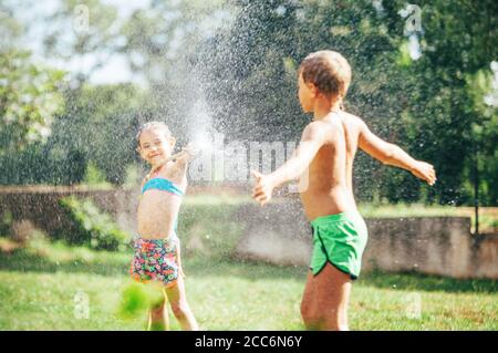 Bruder und Schwester spielen zusammen, erfrischend mit Wasser aus dem Gartenhaus Stockfoto