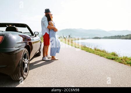 Das verliebte Paar steht in der Nähe des Cabriolets auf dem Malerische Bergstraße Stockfoto