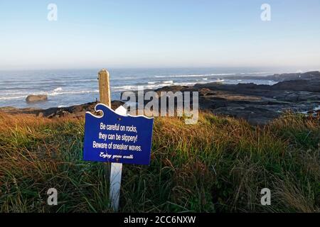 Ein Schild warnt Besucher und Wanderer vor Sneaker-Wellen auf einem Küstenpfad entlang der Pazifikküste von Oregon in der Nähe der Stadt Yachats, Oregon. Stockfoto