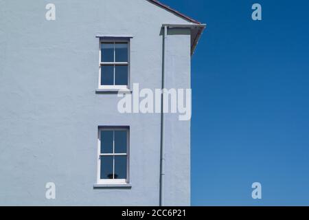 Seitenaussen eines Hauses mit blau pastellfarbenen schlicht gerenderte Wand und zwei Fensterrahmen und schlichtem blauen Himmel. VEREINIGTES KÖNIGREICH Stockfoto