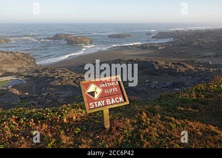 Ein Schild warnt Besucher und Wanderer vor steilen Klippen auf einem Küstenweg entlang der Pazifikküste von Oregon in der Nähe der Stadt Yachats, Oregon. Stockfoto