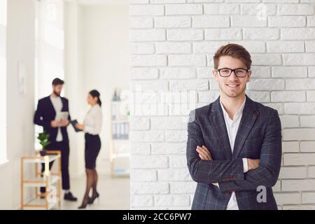 Lächelnder positiver Geschäftsmann in legerer Kleidung, der in einem weißen Büro an einer weißen Wand steht. Stockfoto