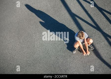 Ein alleinstehender Junge ohne Freunde sitzt auf einem Skateboard. Vorstellung des Konzepts der Einsamkeit von Kindern Stockfoto