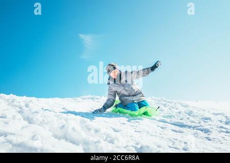 Junge rutscht vom Schneehang herunter. Genießen Sie die Winterrodelzeit Stockfoto