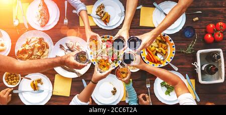 Großes Familienessen. Vertikale Draufsicht auf geservierten Tisch und Hände mit klirenden Kelchen Stockfoto