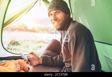 Bärtiger Reisender Mann benutzt sein Mobiltelefon im Zelt sitzend Stockfoto