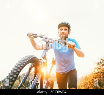 Junger lächelnder Mann, der ein Mountainbike den Hügel hinauf schiebt. Aktive Abenteuerreise mit dem Fahrrad. Stockfoto
